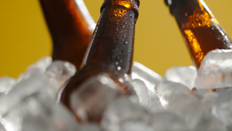 Nahaufnahme-Von-Glasflaschen-Mit-Kaltem-Bier-Oder-Alkoholfreien-Getränken,-Die-In-Einem-Mit-Eis-Gefüllten-Eimer-Vor-Gelbem-Hintergrund-Kühlen